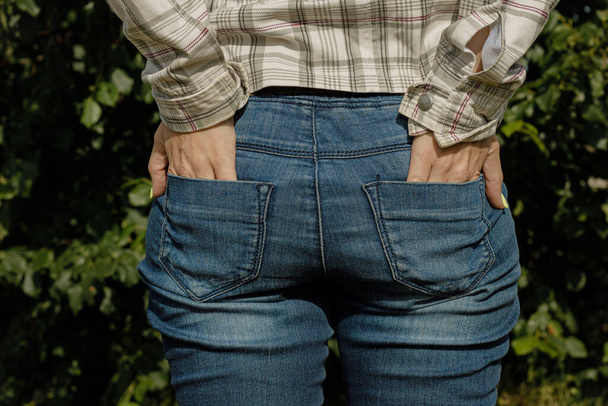 A woman touches her bottom in jeans with her hands. A girl in jeans with a tight ass. Funny outdoor lifestyle portrait of a woman with a beautiful bottom - Fotoğraf, Görsel