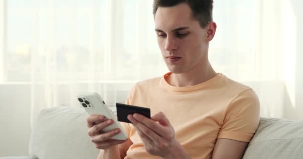 Mutlu ve memnun bir beyaz adam evinin rahatlığından online alışverişe girişiyor. Rahat bir koltukta otururken, bir elinde akıllı telefonunu, diğer elinde de kredi kartını tutuyor.. - Video, Çekim