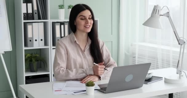 Une femme entrepreneure participe à une réunion en ligne, travaille avec des documents et prend des notes. Elle sourit beaucoup et montre qu'elle aime travailler et se réjouit du processus. - Séquence, vidéo