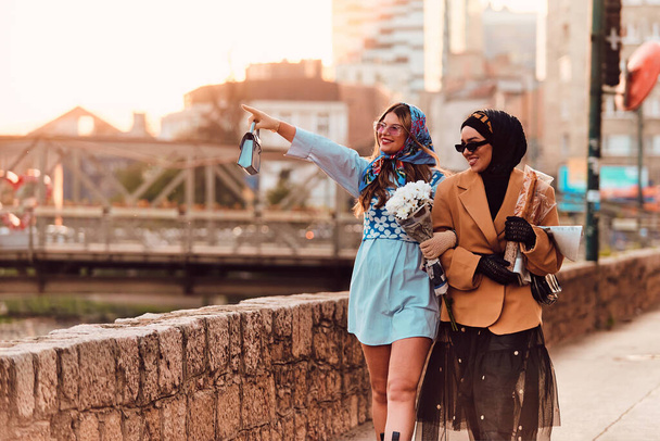 Pari nainen toinen yllään hijabi ja moderni mutta perinteinen mekko, ja toinen sininen mekko ja huivi, kävely yhdessä läpi kaupungin auringonlaskun aikaan. Yksi kuljettaa kimppu ja leipää, kun taas - Valokuva, kuva