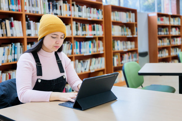 Academic Pursuits: Young Female University Student Studying with her Tablet at the Library (en inglés). Foto de alta calidad - Foto, Imagen