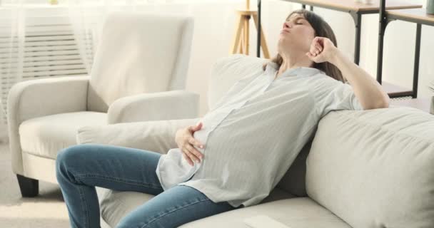 Eine müde Schwangere findet Trost auf einer bequemen Couch. Mit heiterem Gesichtsausdruck und sanfter Berührung streichelt sie liebevoll ihren Babybauch und verleiht ihrem müden Körper Zärtlichkeit und Fürsorge. - Filmmaterial, Video