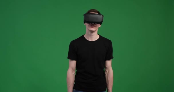 Кавказский человек полностью погружен в виртуальную реальность на ярком зеленом фоне. Нося гарнитуру VR, он погружен в виртуальный мир, его выражение лица источает волнение. - Кадры, видео
