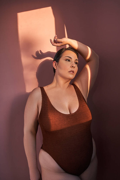 Body positive woman in underwear standing over pink studio background, looking aside at free space. Stop body shaming concept - Фото, изображение