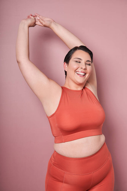 Young, positive, smiling overweight woman training in sportswear, showing biceps, doing exercises against pink studio background. Concept of sport, body-positivity, weight loss, body and health care - Foto, Bild