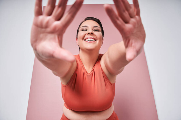 Young caucasian plus size female model stretching on pink background. Concept of sport, healthy lifestyle, body positive, equality - Фото, изображение