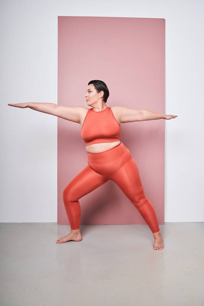 Self-care and well being. Vertical view of the overweight woman training in sportswear against pink studio background. Motivation. Concept of sport, body-positivity, weight loss, body and health care - Fotografie, Obrázek