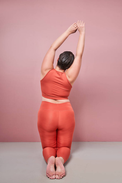 Back view of fat overweight woman wearing sportswear doing fit exercise isolated on studio pink background. Workout sport, fitness and body positive concept - Foto, afbeelding