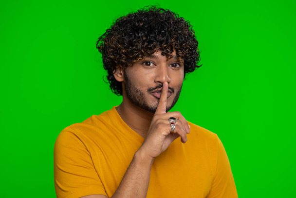Shh be quiet please. Young indian man presses index finger to lips makes silence gesture sign do not tells secret, stop gossip. Handsome bearded hindu guy isolated alone on chroma key background - Photo, Image