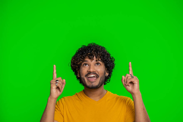 Happy indian man showing thumbs up, pointing empty place over head, advertising area for commercial text inscription, copy-space for goods promotion banner. Hindu guy isolated on chroma key background - 写真・画像