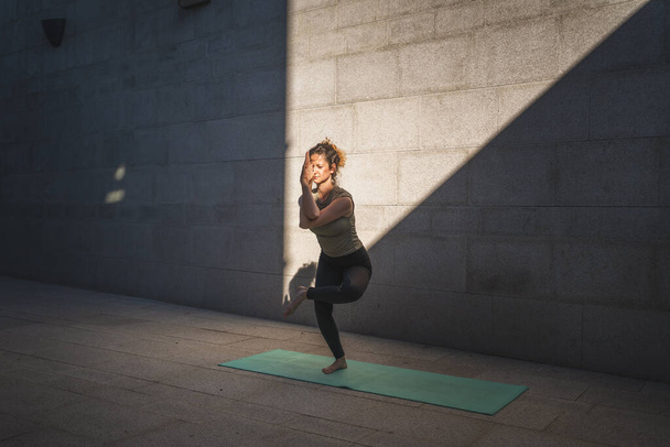 One adult caucasian woman doing yoga practice in summer day outdoor in the city in front of the wall with shadow and sun healthy lifestyle wellbeing concept self care - Fotografie, Obrázek