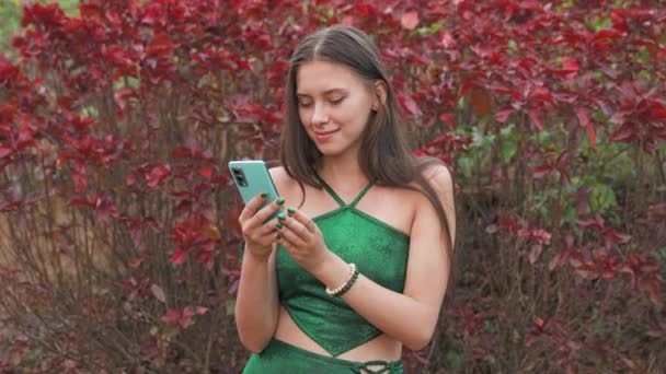 Elinde telefon tutan genç bir kadın tropik çiçeklerin arka planında. Yüksek kalite 4k video kaydı - Video, Çekim