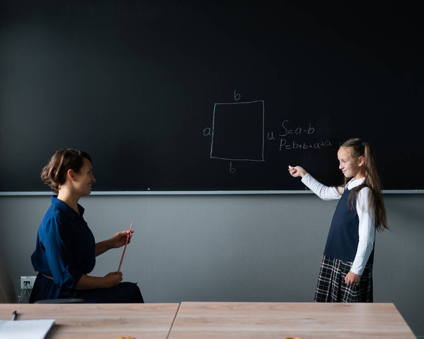 Caucasian little girl answers the question of the female teacher at the blackboard - Fotoğraf, Görsel