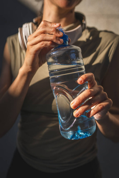 zbliżenie na dłoniach środkowa część nieznanej kaukaskiej kobiety otwarte plastikowe butelki wody podczas stać na zewnątrz w słoneczny dzień - Zdjęcie, obraz