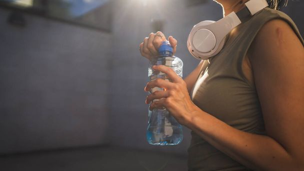 primer plano en las manos sección media de mujer caucásica desconocida abierta botella de plástico de agua, mientras que de pie al aire libre en el día soleado - Foto, imagen