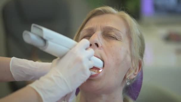 De tandarts onderzoekt de tanden van een oudere dame in een moderne kliniek, het verstrekken van haar met uitgebreide tandheelkundige zorg. - Video