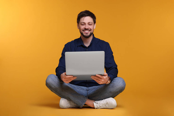 Happy man with laptop sitting on yellow background - Фото, изображение