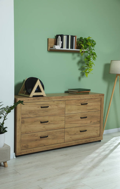New wooden chest of drawers, plants and lamp near green wall in stylish room - Foto, Bild