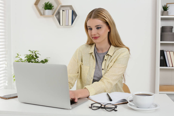 Home workplace. Woman working on laptop at white desk in room - Photo, Image