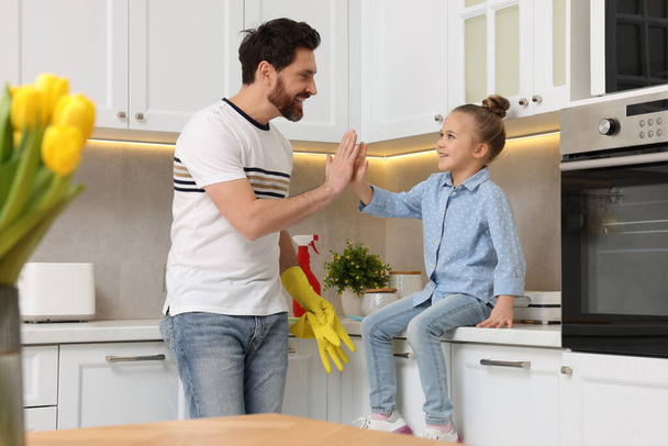 Spring cleaning. Father and daughter giving high five in kitchen - Foto, afbeelding
