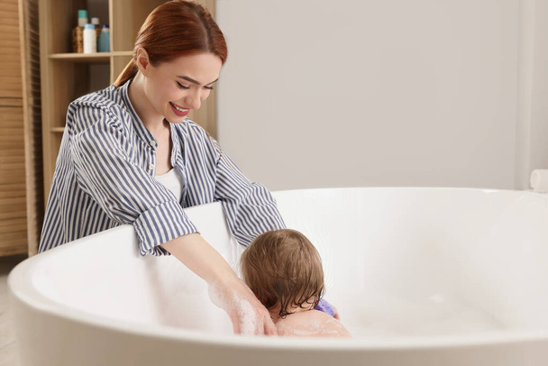 Mother washing her little baby in tub at home - Фото, зображення