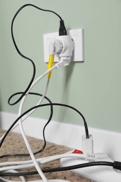 Different electrical plugs in socket and power strip on floor indoors, closeup - Фото, изображение