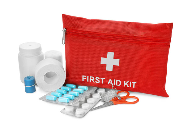 Red first aid kit, scissors, pins, pills, medical plaster and elastic bandage isolated on white - Foto, Imagem