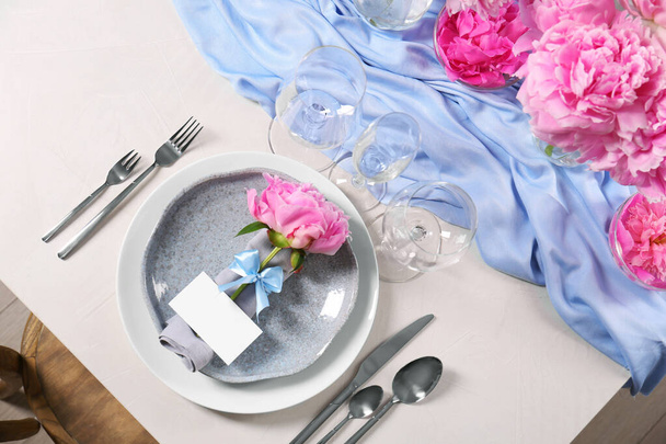 Stylish table setting with beautiful peonies, napkin and blank card, above view - Фото, изображение