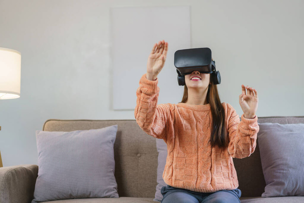 家庭での生活の中でビデオゲームを見るために仮想現実ゴーグルで経験を楽しむ女性. - 写真・画像
