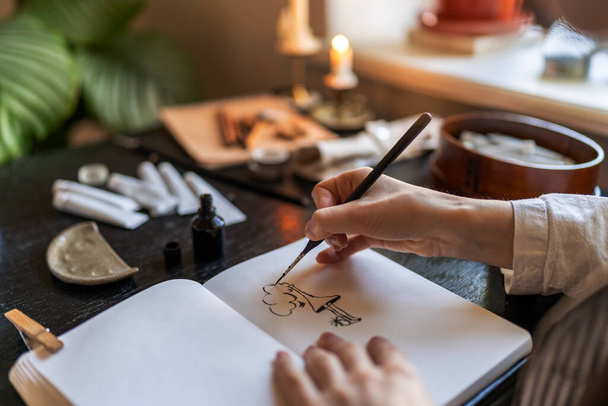 Zbliżenie artysty trzymającego rysunek wiecznego pióra tuszem, siedzącego przy stole z szkicownikiem i narzędziami malarskimi, rysującego w domu, tworzącego dzieła sztuki. Kreatywni ludzie i koncepcja inspiracji - Zdjęcie, obraz