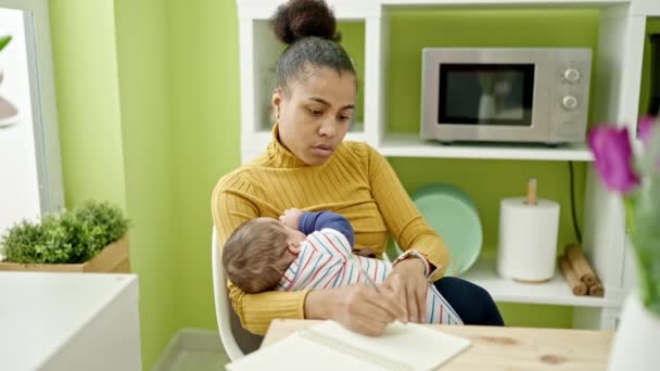 Mother and son writing notes while breastfeeding baby at dinning room - Footage, Video