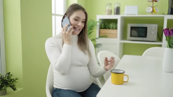 Nuori raskaana oleva nainen puhuu älypuhelimella juoden kahvia ruokasalissa - Materiaali, video