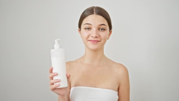 Menina bonita jovem sorrindo confiante segurando garrafa creme sobre fundo branco isolado - Filmagem, Vídeo