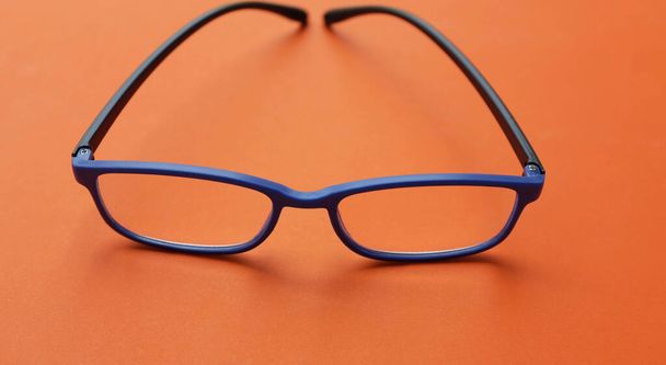 close up and flat lay a modern glasses,eyewear,spectacles,spectacles,glasses blue frames fashion for men and women over the orange background - Foto, Imagem
