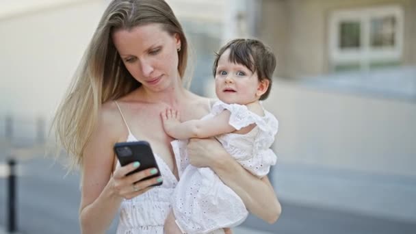 Madre e figlia che si abbracciano usando lo smartphone in strada - Filmati, video
