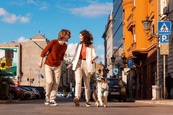 Νεαρό ζευγάρι Καυκάσιων με κατοικίδιο που περπατάει στην πόλη. Εκπαίδευση καθαρόαιμο Aussie σκυλί. - Φωτογραφία, εικόνα