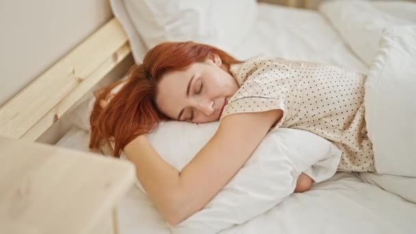 Młoda ruda kobieta leży na łóżku przytulając poduszkę śpi w sypialni - Materiał filmowy, wideo