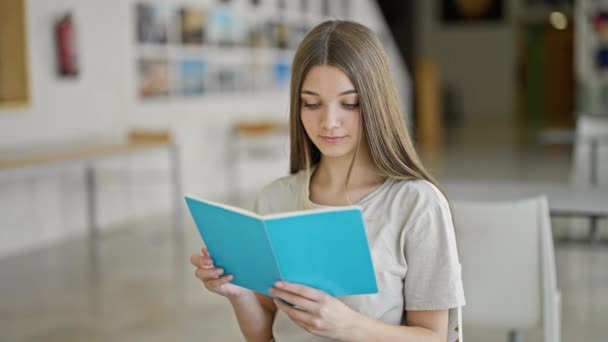 Молодая красивая студентка читает книги в библиотеке - Кадры, видео