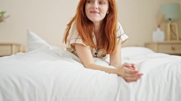 Молодая рыжая женщина касается волос, лежащих на кровати, улыбаясь в спальне. - Кадры, видео