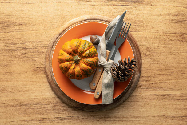 Um prato com talheres é decorado para Ação de Graças com abóboras e produtos de outono em uma mesa de madeira, vista superior - Foto, Imagem