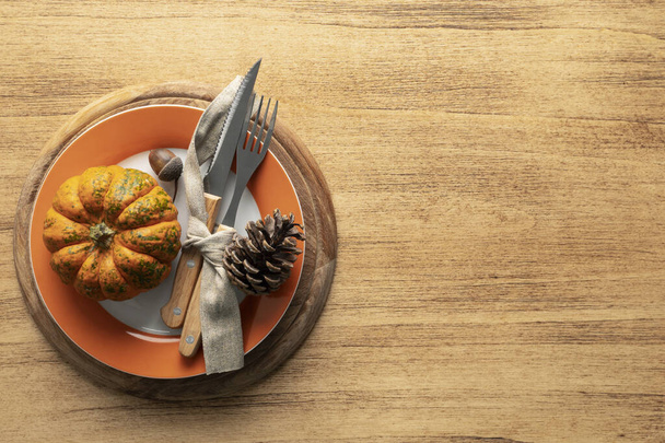 A plate with cutlery is decorated for Thanksgiving with pumpkins and autumn products on a wooden table, top view - Photo, Image