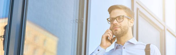 İş görüşmesi. Mavi gömlekli yakışıklı beyaz iş adamı dışarıda dikilirken telefonla konuşuyor. - Fotoğraf, Görsel