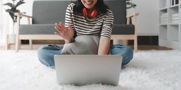 Young asian relaxed smiling pretty woman relaxing with laptop at home. Female feeling joy enjoying with mobile phone on cozy couch. - 写真・画像