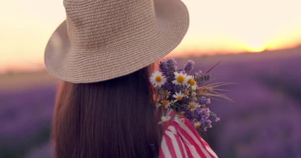 Piękna kobieta z sukienka i kapelusz korzystających kolor lawendy wierszy w niekończącym się polu kwitnienia. Dziewczyna z bukietem kwiatów oglądać zachód słońca - Materiał filmowy, wideo