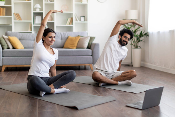 Fitness Online. Happy Young Indian Couple Doing Sports At Home With Laptop, Fit Eastern Man And Woman Watching Online Lessons And Exercising On Mat In Living Room, Making Domestic Workout, Copy Space - Photo, Image