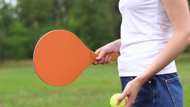 自然を背景に木製ラケットでパドルボールを再生します。女の子の手にテニスとボールを再生するための木製のパドル。屋外ゲーム。閉鎖 - 映像、動画