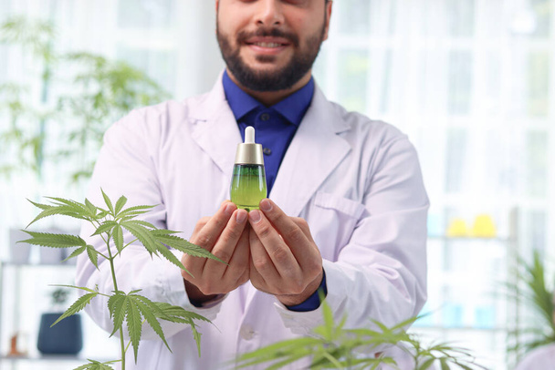 Scientist man holding marijuana oil in laboratory, biochemist doing experiment with hemp leaf, pharmacist extract aromatic cannabis oil in lab, medical researcher work for alternative herb medicine. - 写真・画像