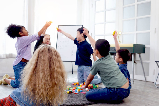 Group of primary school children study and play together in classroom with teacher, diverse students sit on floor while do activities and have fun, kid education, variety and diversity classroom. - Φωτογραφία, εικόνα