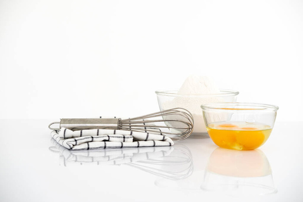 Baking concept. Egg yolk Bowl with a whisk and dishcloth on white table over white background with copy space. - Photo, Image