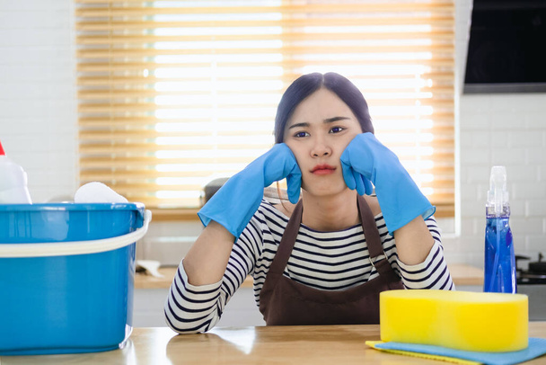 Tired young woman sitting in kitchen room with cleaning products and equipment, Housework concept - Foto, imagen